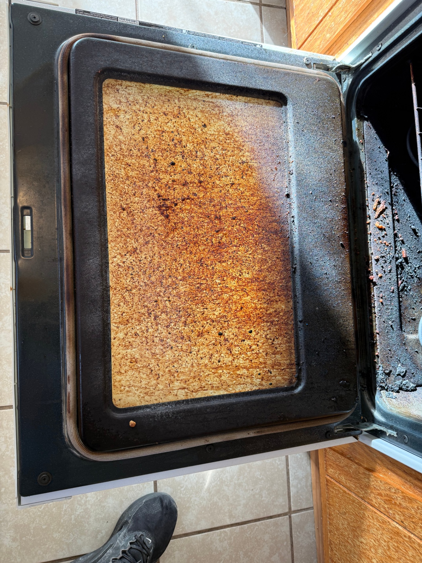 Oven door interior caked with baked-on grease and burnt residue